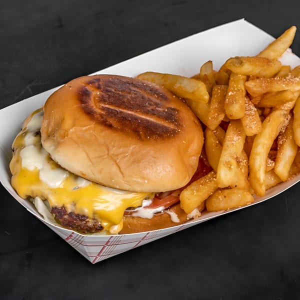 Cheeseburger with melted cheese, tomatoes, and sauce, served with seasoned fries in a paper tray.