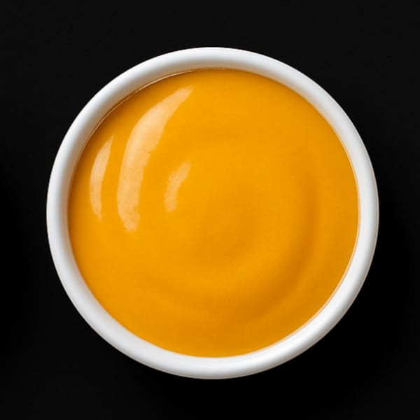 Overhead view of a white ramekin filled with bright orange House Of Wings sauce on a black background.