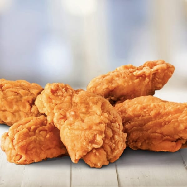 Crispy, golden-brown boneless chicken wings from House Of Wings, piled on a white wooden surface.