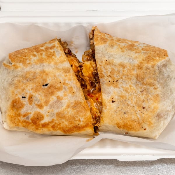 A large, grilled burrito cut in half, revealing a savory filling of meat and cheese.