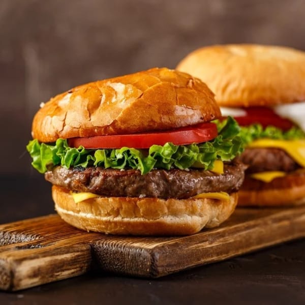 Two juicy burgers with lettuce, tomato, and cheese on a wooden board.