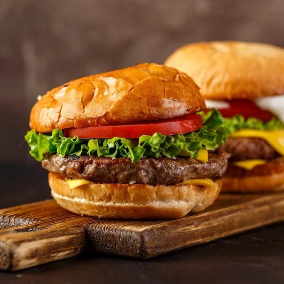 Two juicy burgers with lettuce, tomato, and cheese on a wooden board.